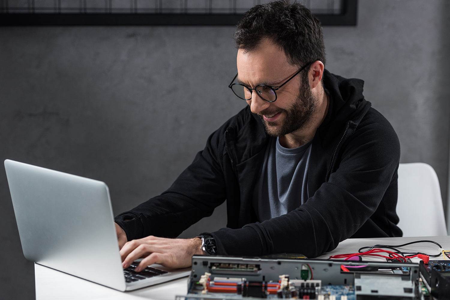 smiling man using laptop against broken pc on table